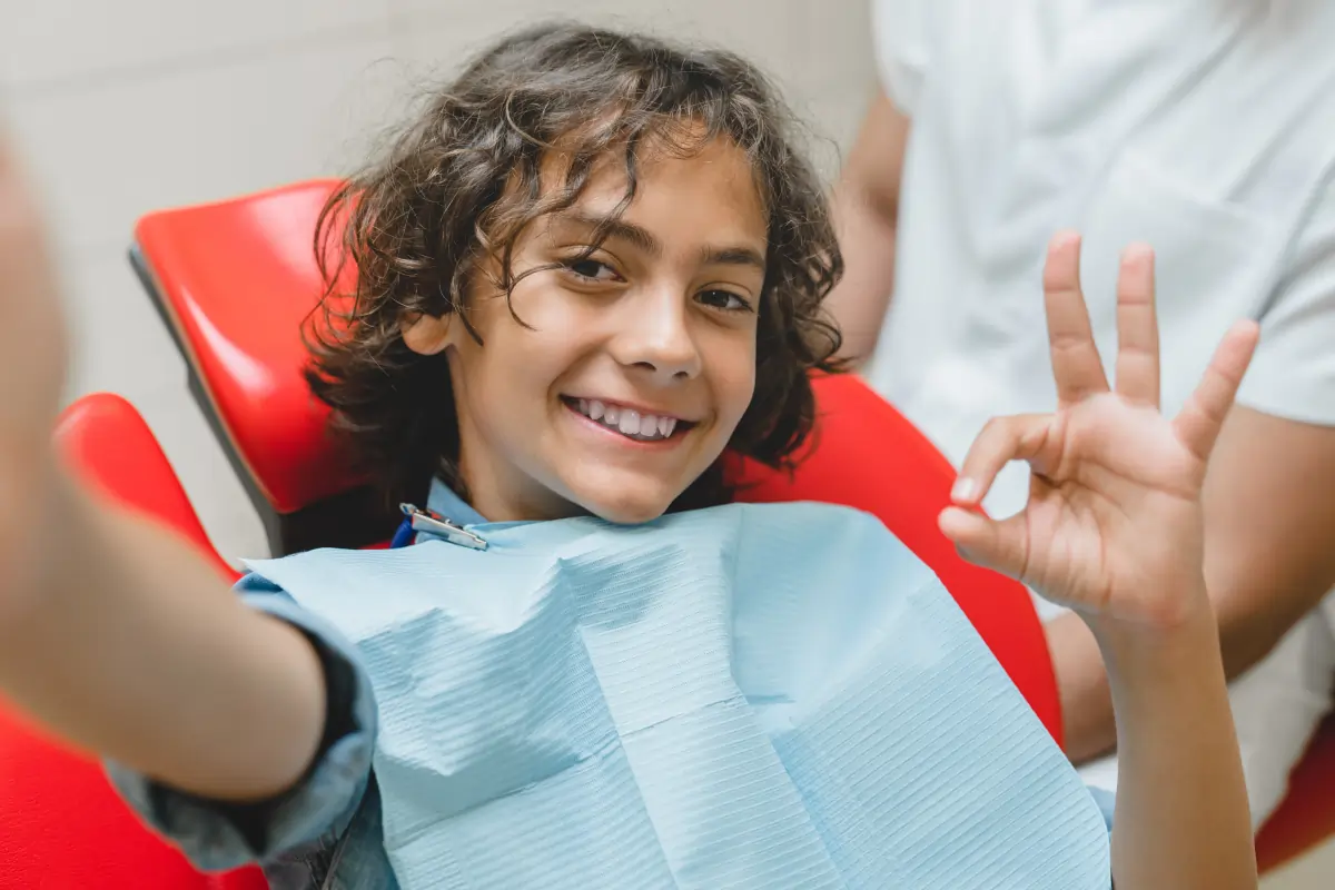 Young child in red dental chair smiling and waving at pediatric dental office.