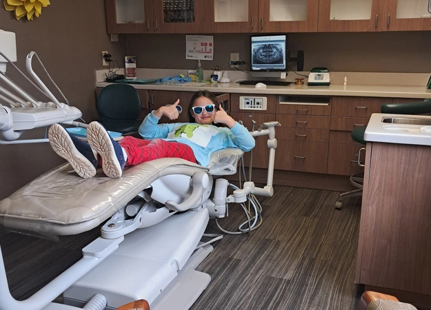 Young child receiving dental treatment in pediatric dental operatory with overhead light and equipment.