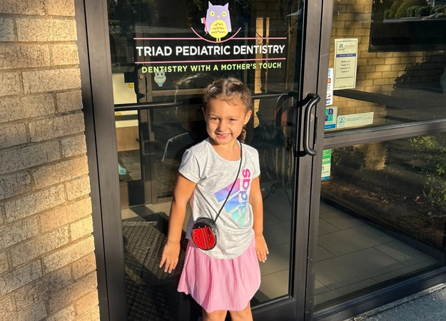 Young girl smiling at entrance of Triad Pediatric Dentistry office doorway.