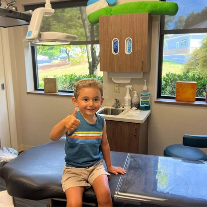 Young child sitting on dental chair in pediatric dentistry office examination room.
