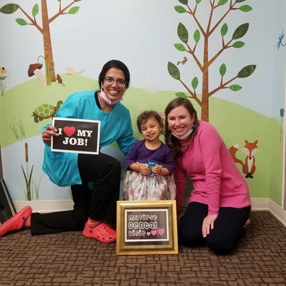 Three people celebrate with "Great Job!" sign and award plaque against colorful mural backdrop.