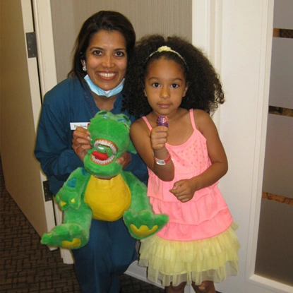 Two young girls holding green stuffed frog toy in dental office hallway.