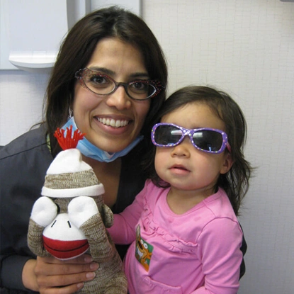 Young woman and child wearing sunglasses holding puppet toy in dental office setting.