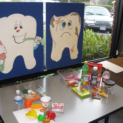 Dental health education display with happy and sad tooth characters and sugar products on table.