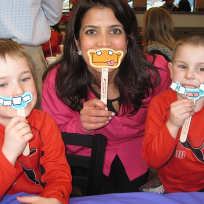 Woman and two children holding decorative tooth props, smiling at dental office.