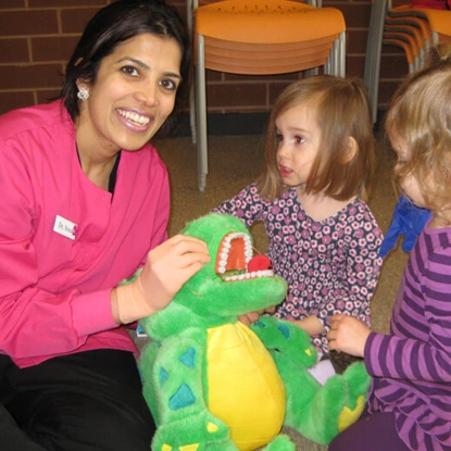 Pediatric dentist in pink scrubs playing with children and interactive toy during dental visit.