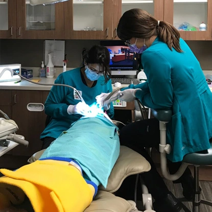Pediatric dentist examining young patient's teeth in modern dental office with assistant.