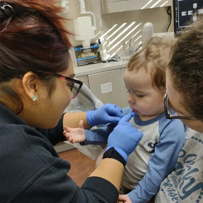 Pediatric dentist in blue gloves examines young child's teeth in dental office.