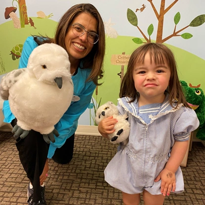 Woman and young girl holding stuffed animals in pediatric dental office with colorful wall decorations.