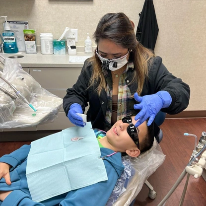 Pediatric dentist examining young patient's teeth in clinical dental office setting.