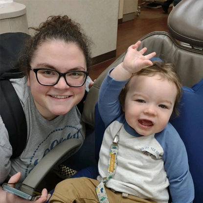 Smiling dental professional with young toddler in dental office setting.