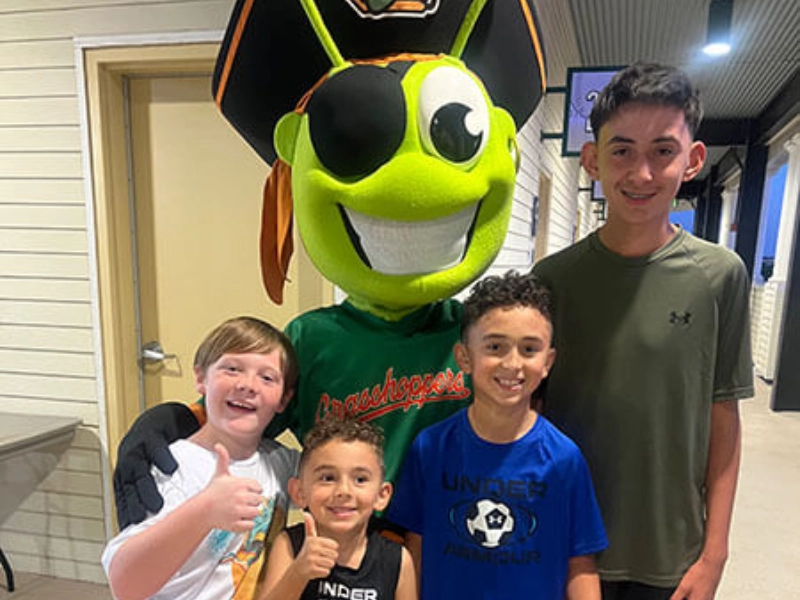Family poses with large green mascot character at pediatric dental office.