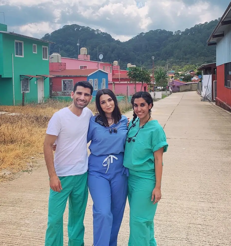 Three healthcare professionals in scrubs standing together on a rural mountain village road.