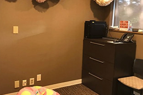 Modern dental office waiting room with black dresser, tan walls, and decorative elements.