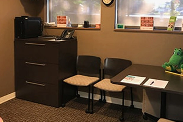 Pediatric dental office waiting area with black furniture, chairs, and educational materials on walls.