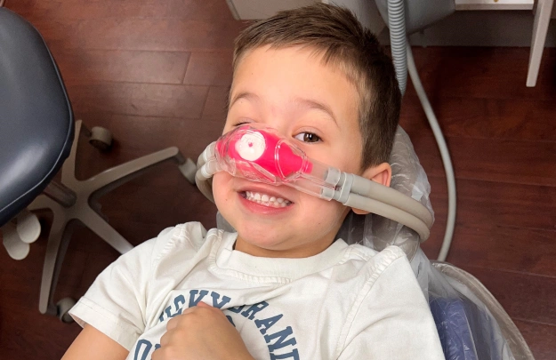 Young child wearing pink play glasses in dental office chair during visit.