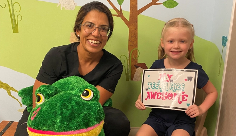 Adult and child holding green frog plush toy and drawing in dental office setting.