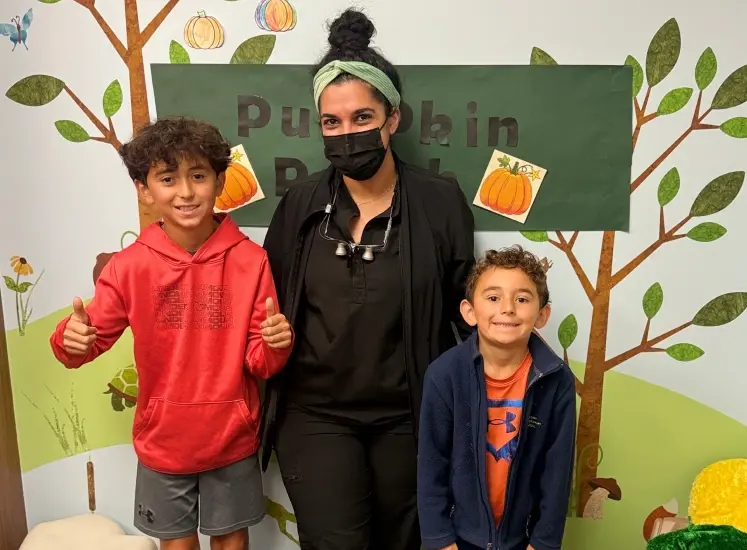 Female dental professional with two young patients smiling together in office.